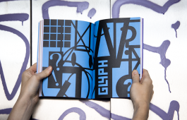 Eine aufgeschlagene Buchdoppelseite zeigt mehrere Symbole und Buchstaben, die von Frauen und Queers gestaltet wurden 